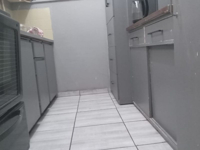 A compact kitchen featuring built-in cabinetry, tiled flooring, and a built-in oven, offering a functional layout in need of cosmetic updates.