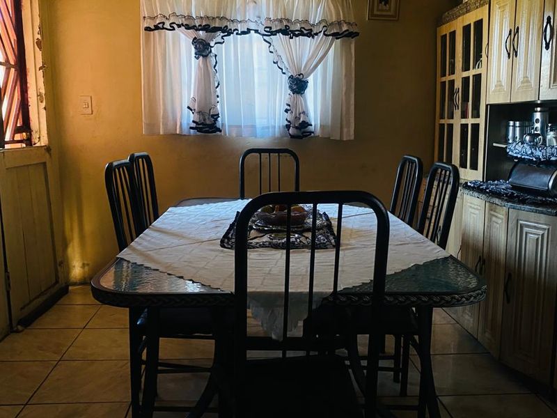 A dining area featuring tiled flooring and built-in wooden cabinetry with granite countertops, showing signs of age and dated finishes.