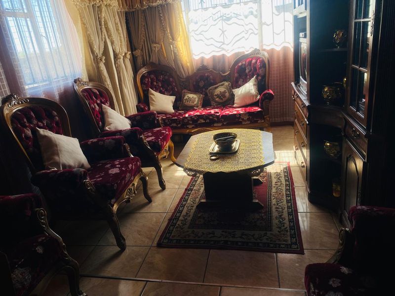 A living room featuring tiled flooring and large windows with security bars, currently furnished with traditional seating.