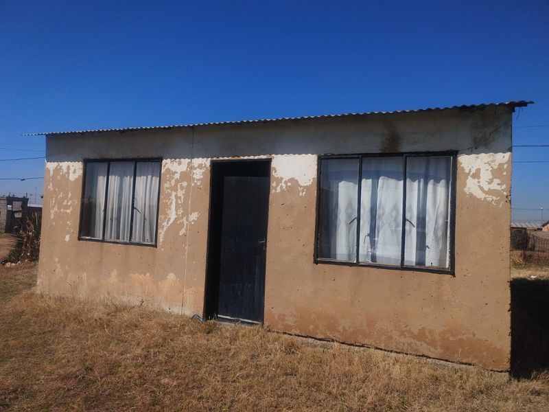 A single-story residential structure featuring a corrugated metal roof and sliding windows, currently showing significant exterior paint deterioration and weathering.