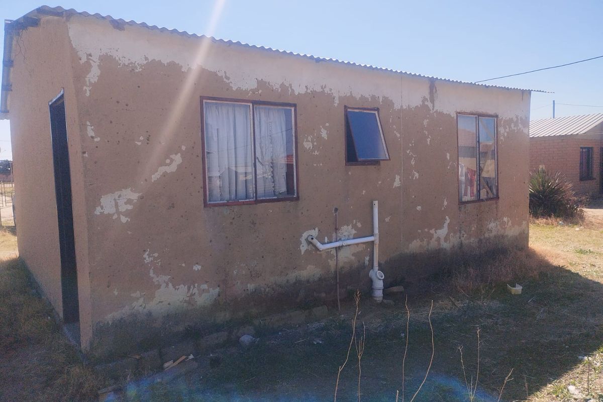Exterior view of a small residential structure showing significant wear to the exterior wall finish and exposed plumbing fixtures.