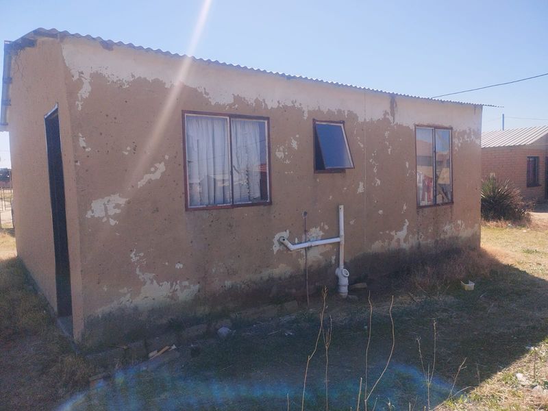 Exterior view of a small residential structure showing significant wear to the exterior wall finish and exposed plumbing fixtures.