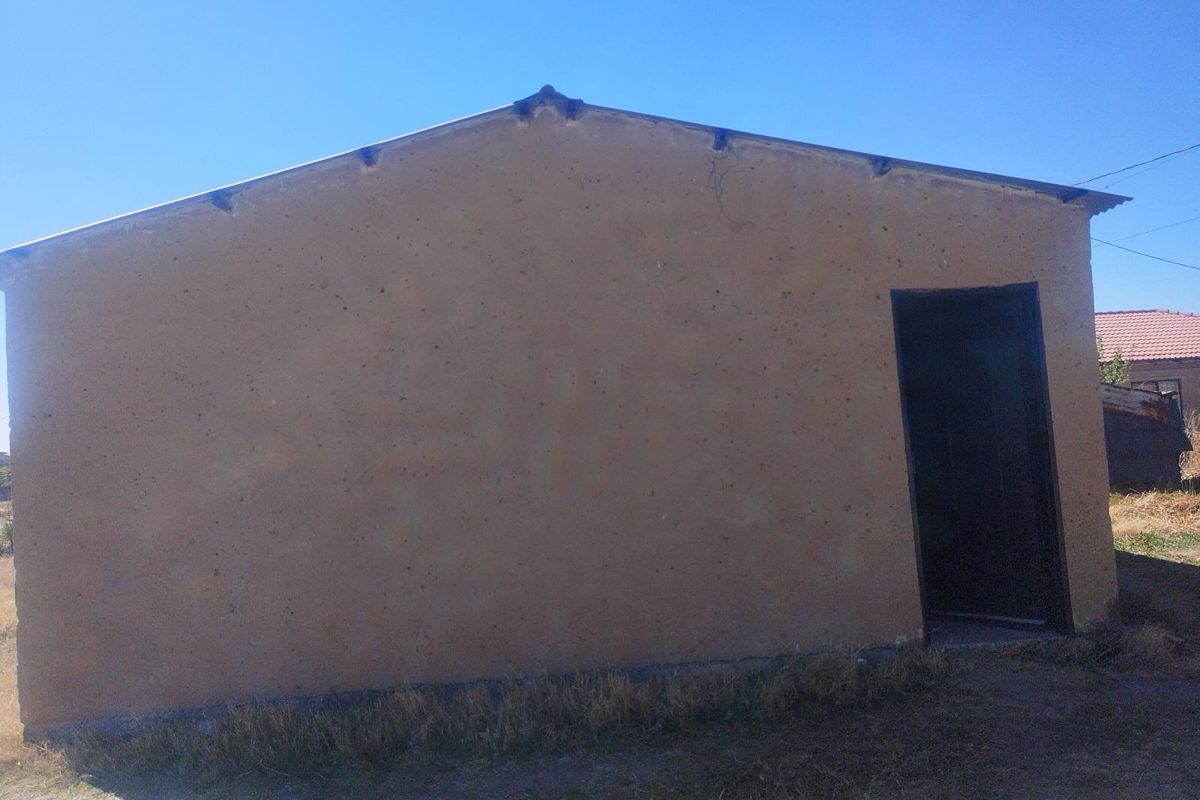 A view of the rear exterior elevation of the house featuring a simple plastered wall and metal roofing.