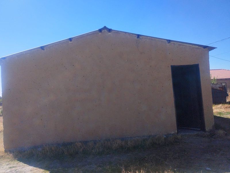 A view of the rear exterior elevation of the house featuring a simple plastered wall and metal roofing.