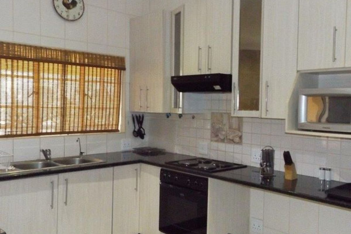 Functional kitchen featuring light-toned cabinetry, dark granite countertops, built-in oven, hob, extractor fan, and a double basin sink with tiled backsplash.