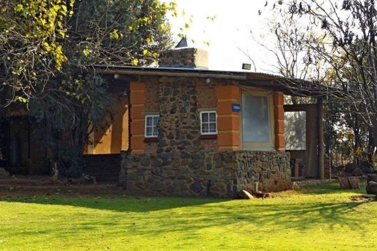 A rustic stone-clad outbuilding featuring a chimney and a covered patio area, set within a spacious garden environment.