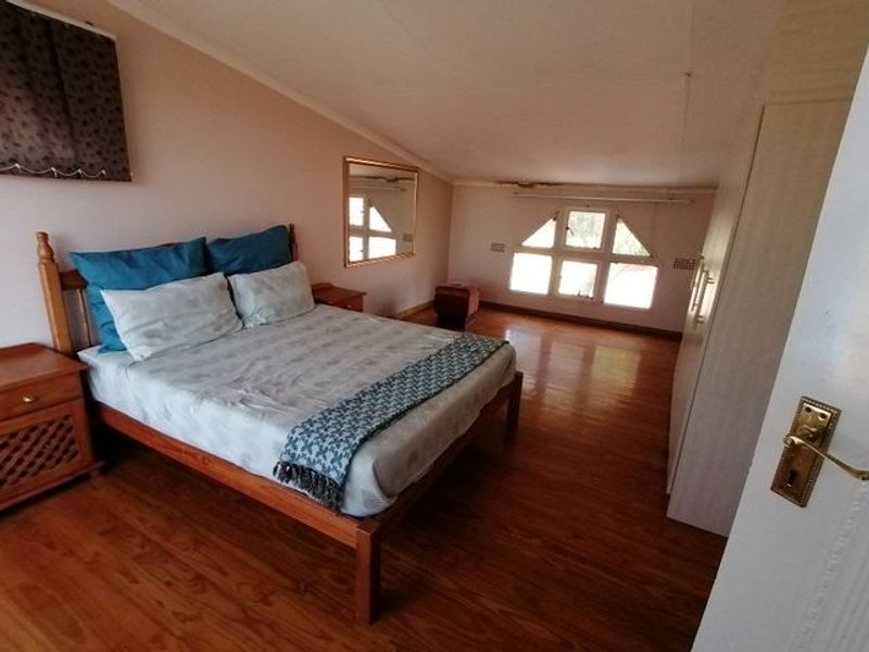 Spacious bedroom featuring laminate flooring, sloped ceilings, and built-in cupboards, offering a functional layout with natural light from the casement windows.