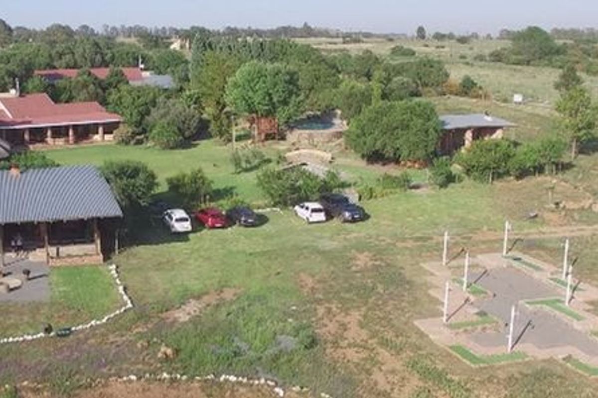 Aerial view of a small holding property featuring multiple buildings, a swimming pool, expansive garden areas, and a paved driveway.