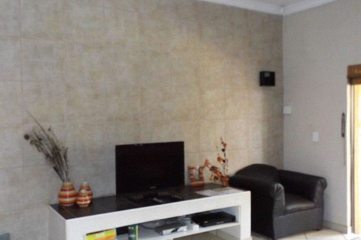 A living room area featuring a tiled accent wall, ceramic floor tiles, and coved ceiling cornicing.
