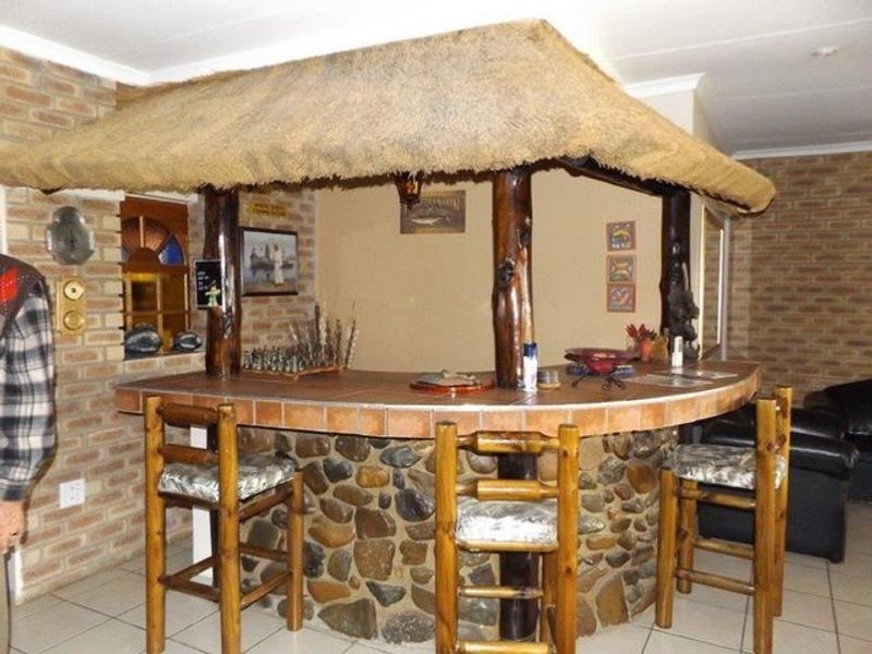 A rustic indoor bar area featuring a stone-clad counter, thatched roof canopy, and exposed brick walls, creating a traditional entertainment space.