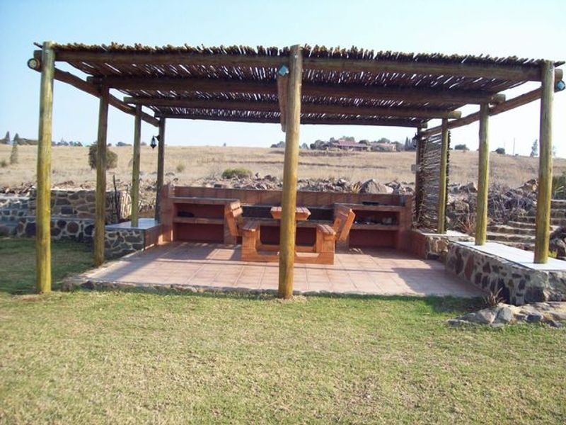 Outdoor entertainment area featuring a thatched pergola, built-in braai, and stone masonry detailing, set within a spacious garden environment.