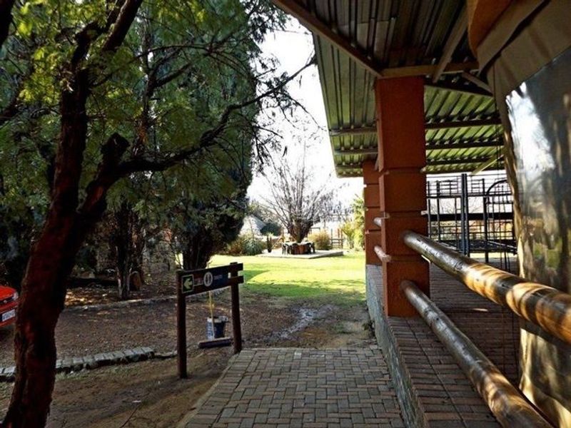 A covered outdoor patio area featuring brick pillars, timber railings, and a paved walkway overlooking the garden grounds.