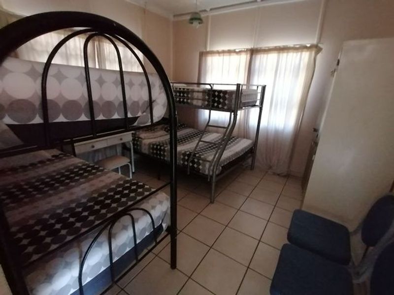 A functional bedroom featuring tiled flooring and large windows with curtain rails, providing ample natural light.