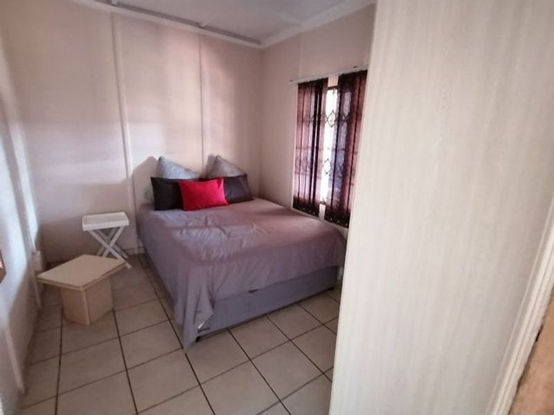 A compact bedroom featuring tiled flooring and a window fitted with security bars.