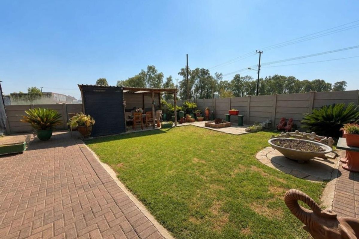 A well-maintained rear garden featuring a paved patio area, a covered outdoor entertainment space, and a lawn enclosed by precast concrete boundary walls.