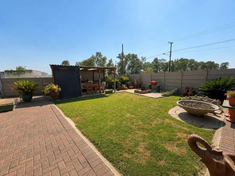 A well-maintained rear garden featuring a paved patio area, a covered outdoor entertainment space, and a lawn enclosed by precast concrete boundary walls.