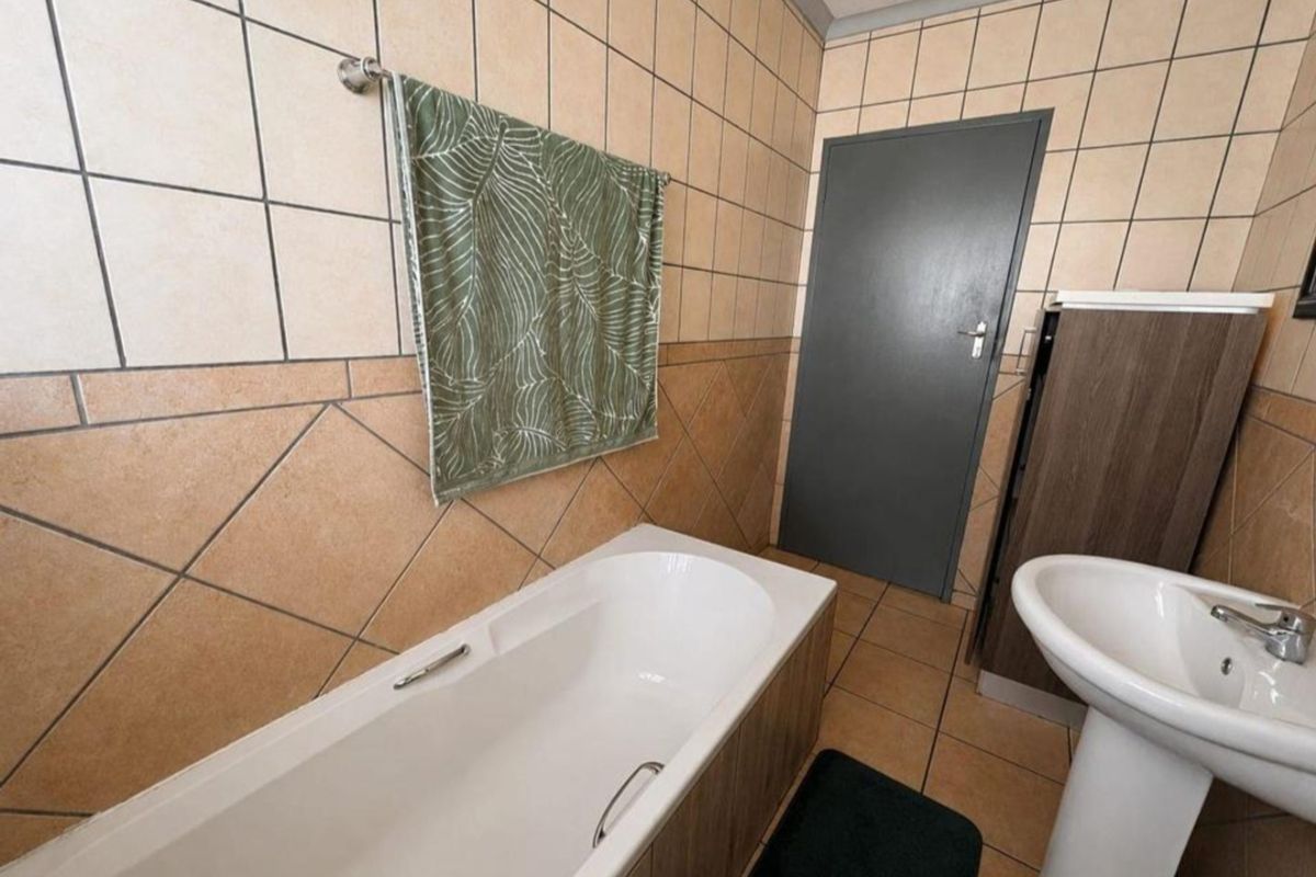 A functional bathroom featuring a bathtub, pedestal basin, and neutral tiled finishes throughout.