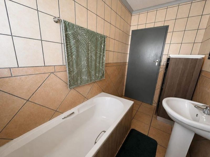 A functional bathroom featuring a bathtub, pedestal basin, and neutral tiled finishes throughout.