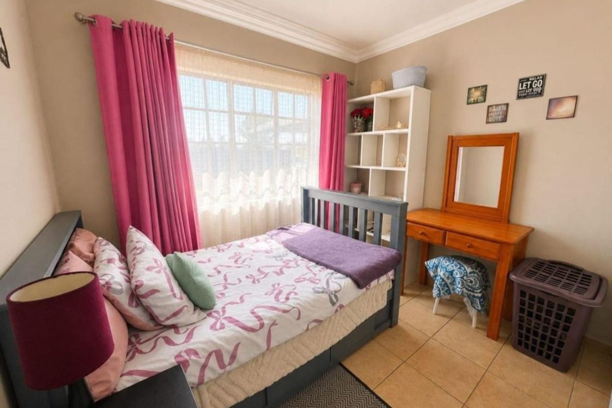 A cozy bedroom featuring tiled flooring, neutral wall tones, and a window with curtains, providing a functional and comfortable living space.