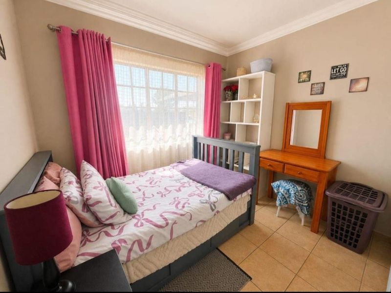 A cozy bedroom featuring tiled flooring, neutral wall tones, and a window with curtains, providing a functional and comfortable living space.