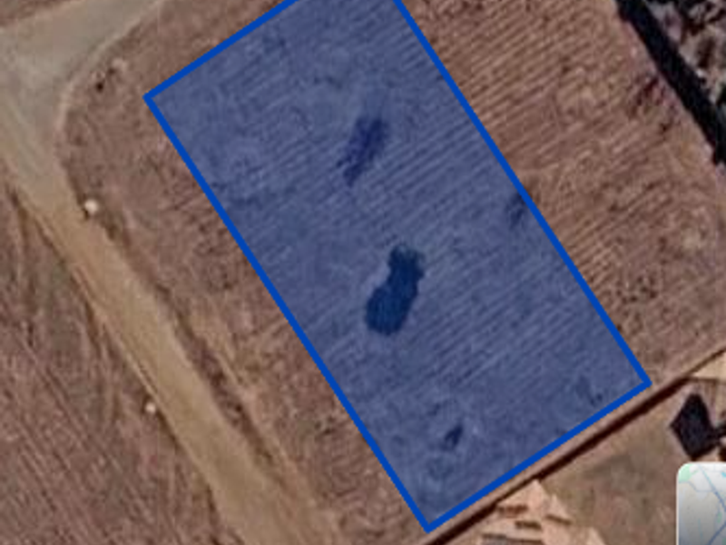 An aerial view of a vacant residential plot of land, highlighting the property boundaries and surrounding terrain.