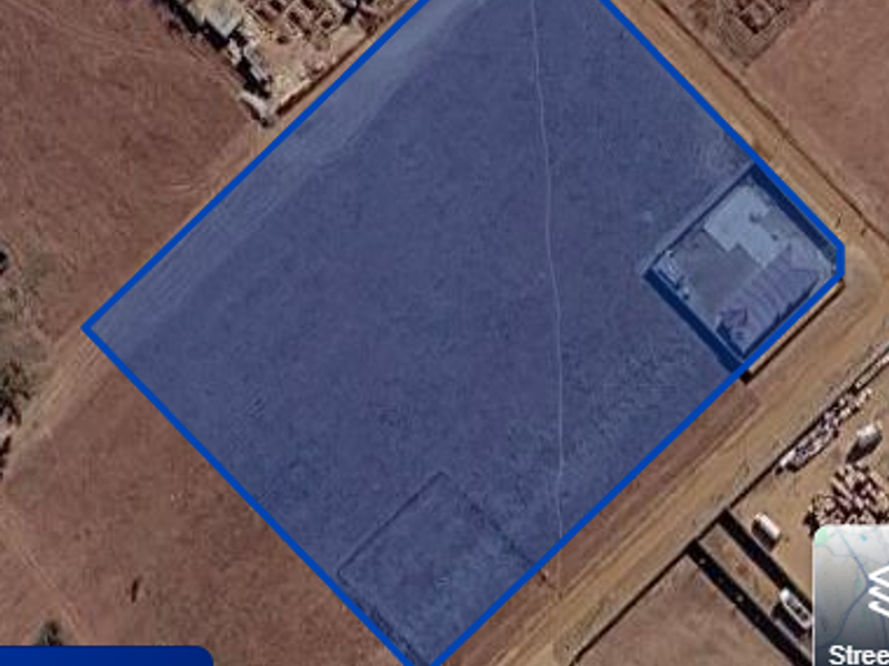An aerial view of a vacant residential plot with boundary lines highlighted, showing the undeveloped land and surrounding area.