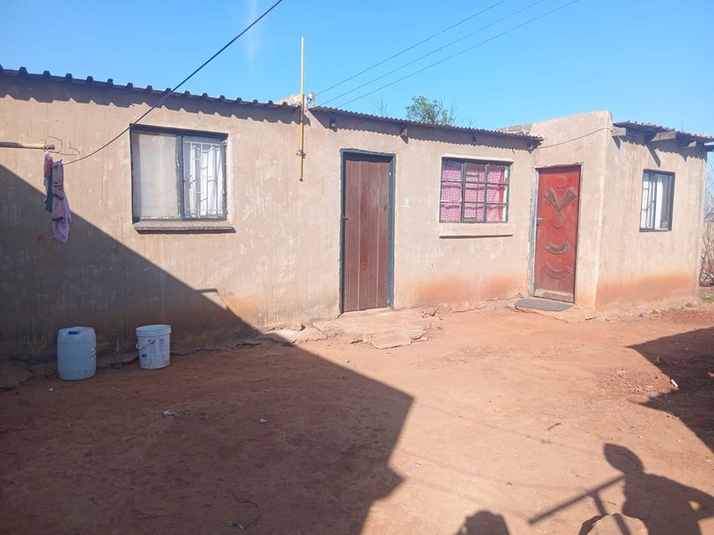 A view of the rear exterior of a modest single-story dwelling featuring a corrugated metal roof and basic timber door access.