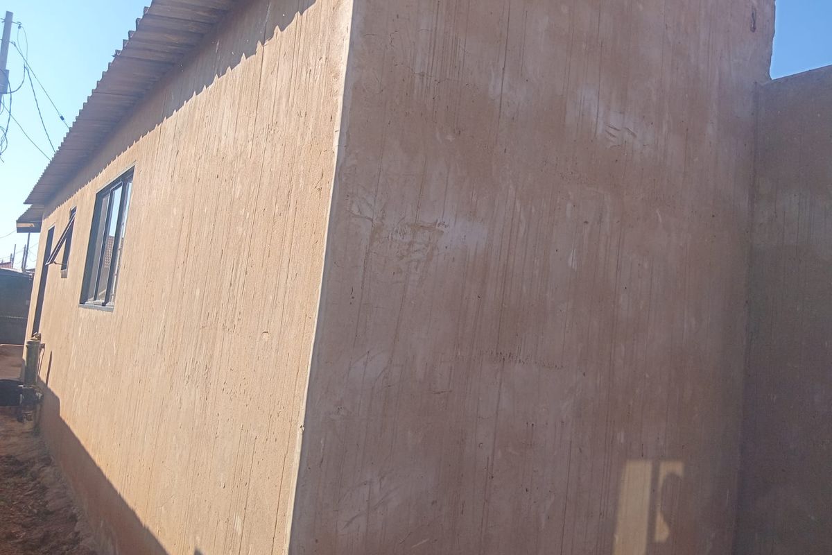 Side view of the property showing an unfinished cement plastered wall and corrugated metal roofing.
