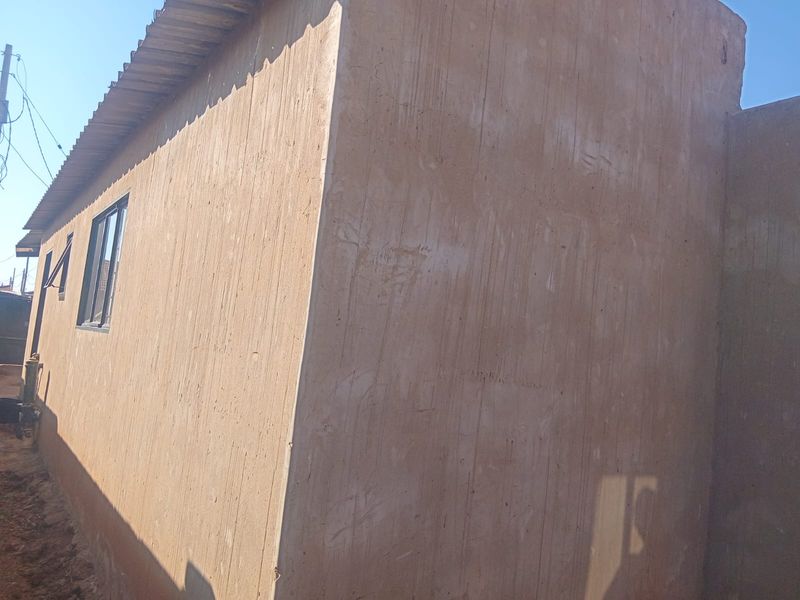 Side view of the property showing an unfinished cement plastered wall and corrugated metal roofing.