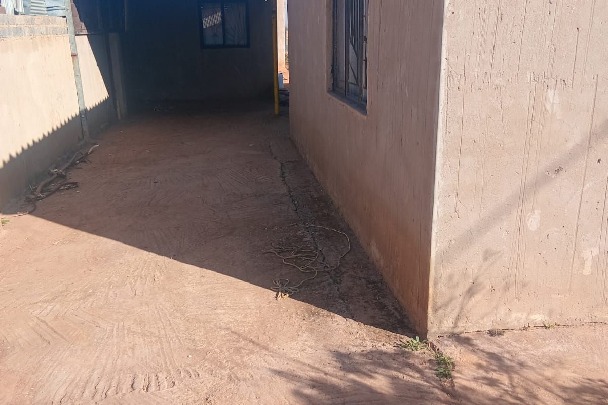 Side exterior view of the property featuring a concrete driveway, metal window frames, and a covered outdoor area with a corrugated metal roof.