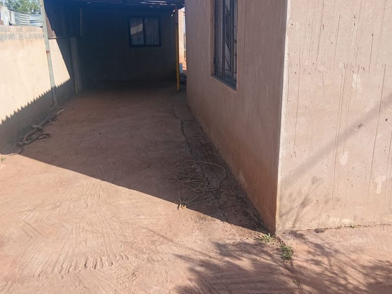 Side exterior view of the property featuring a concrete driveway, metal window frames, and a covered outdoor area with a corrugated metal roof.