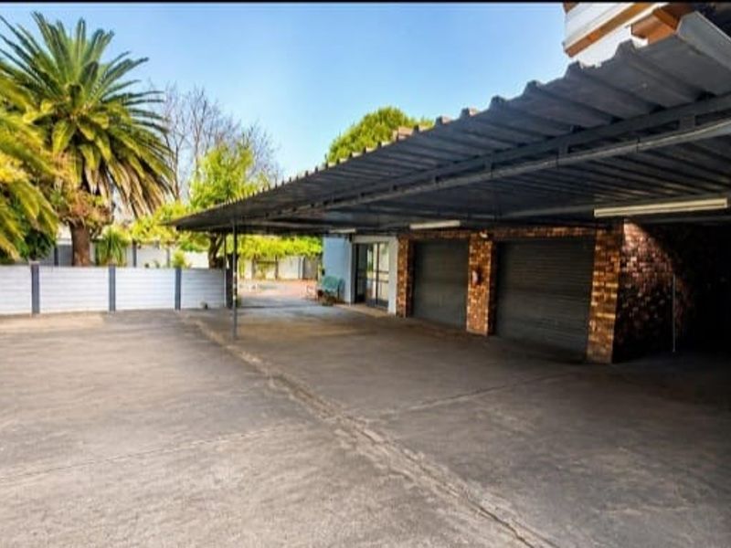 Spacious paved driveway area featuring a large covered carport and multiple secure garage bays with roller doors.