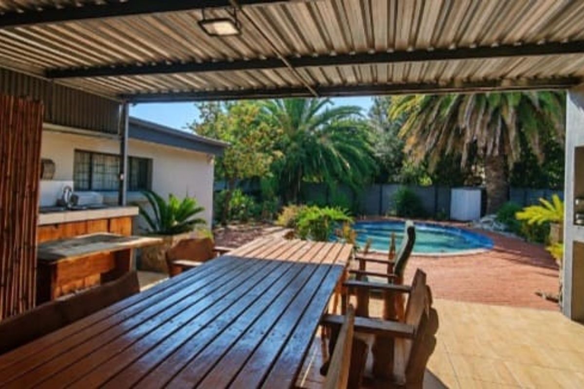 Covered outdoor patio featuring a built-in braai, sink, and tiled flooring, overlooking a private swimming pool and garden area.