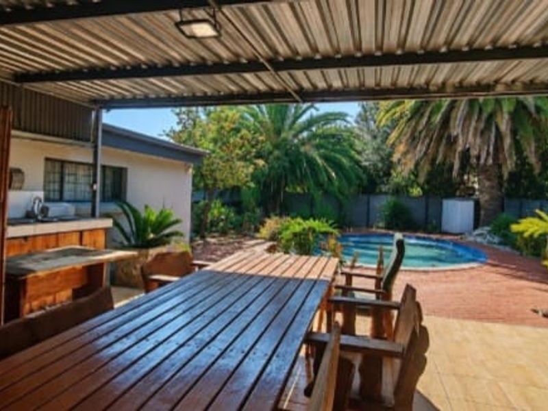 Covered outdoor patio featuring a built-in braai, sink, and tiled flooring, overlooking a private swimming pool and garden area.