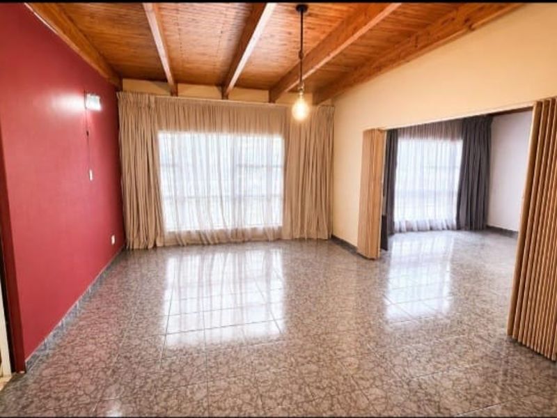 Spacious living area featuring exposed timber beam ceilings, ceramic tile flooring, and a folding room divider connecting to an adjacent space.