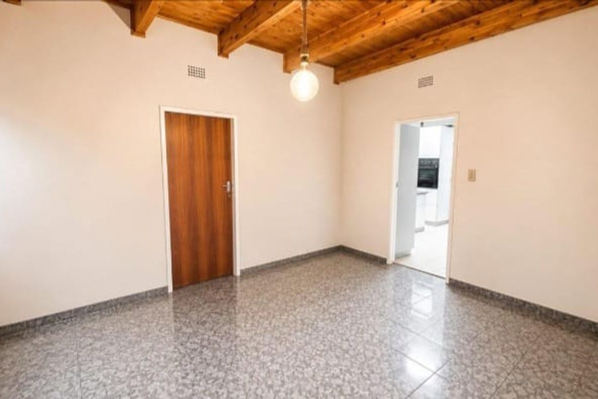 An empty living area featuring exposed timber ceiling beams, tiled flooring, and a solid wood door, offering a clean canvas for interior design.