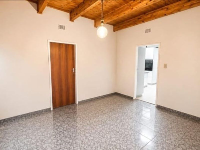 An empty living area featuring exposed timber ceiling beams, tiled flooring, and a solid wood door, offering a clean canvas for interior design.