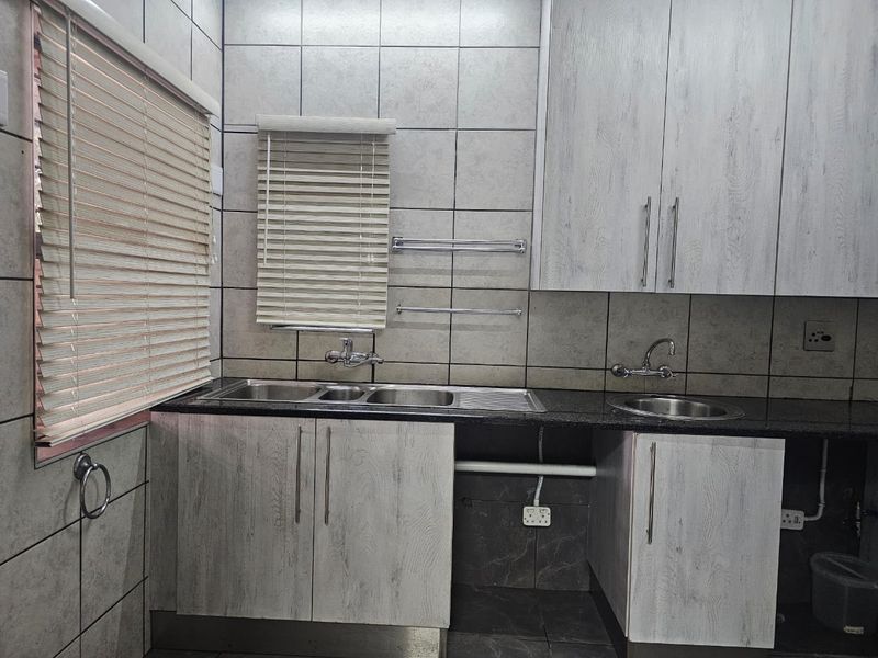 A functional scullery area featuring dual stainless steel sinks, granite countertops, and ample built-in cabinetry with modern grey wood-grain finishes.