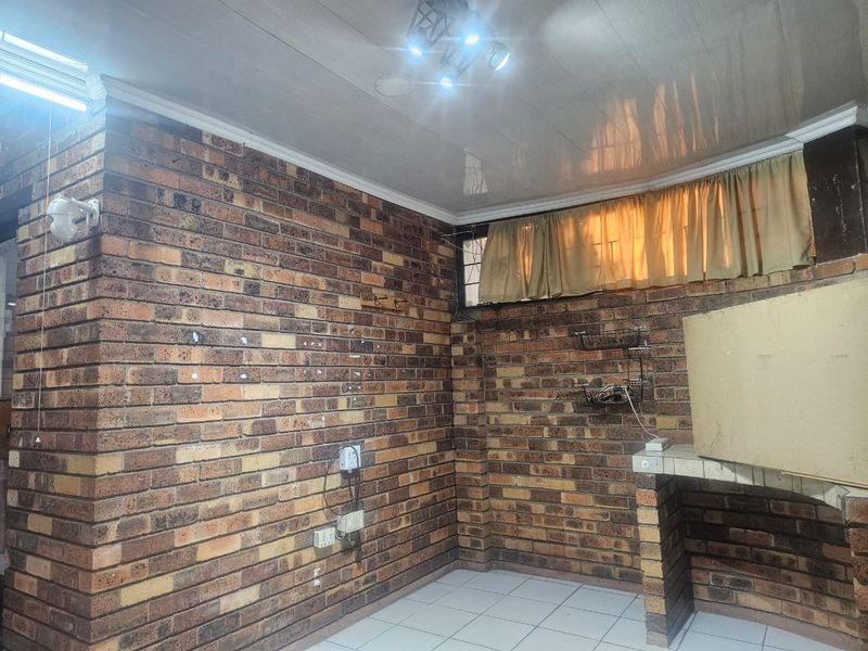 A rustic kitchen area featuring exposed brick walls, tiled flooring, and a built-in brick counter, offering a blank canvas for renovation.