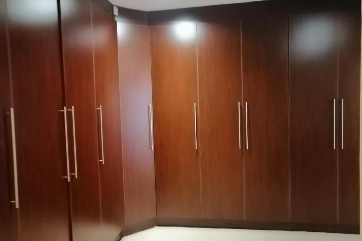 A bedroom featuring extensive floor-to-ceiling built-in wooden cabinetry with modern metal handles, providing ample integrated storage space.