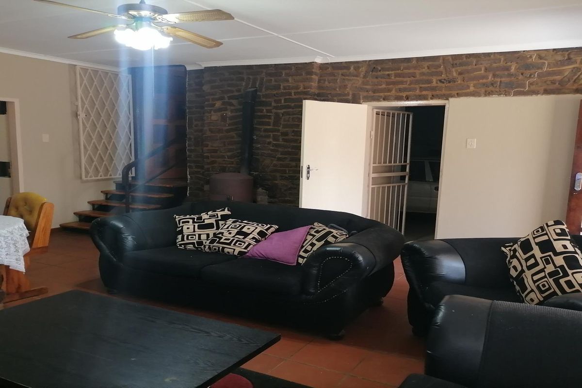 Spacious living area featuring a rustic exposed brick wall, a wood-burning stove, and a wooden staircase leading to the upper level.