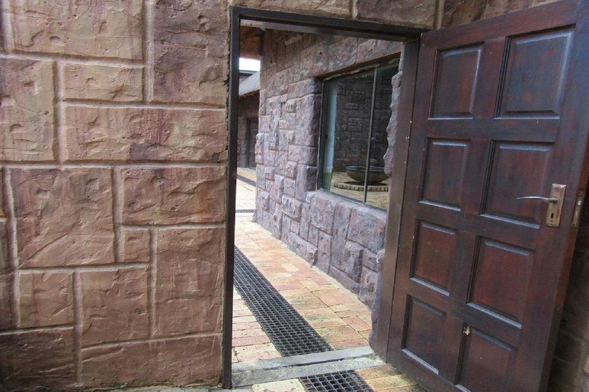 An exterior view showing a stone-clad facade with a wooden door leading into a paved walkway area.