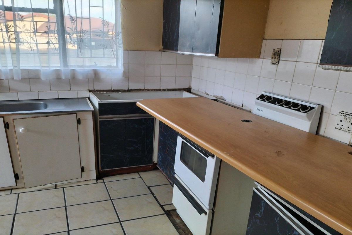 A dated kitchen featuring tiled flooring, laminate countertops, and built-in cabinetry, requiring modernization and repair to restore functionality.