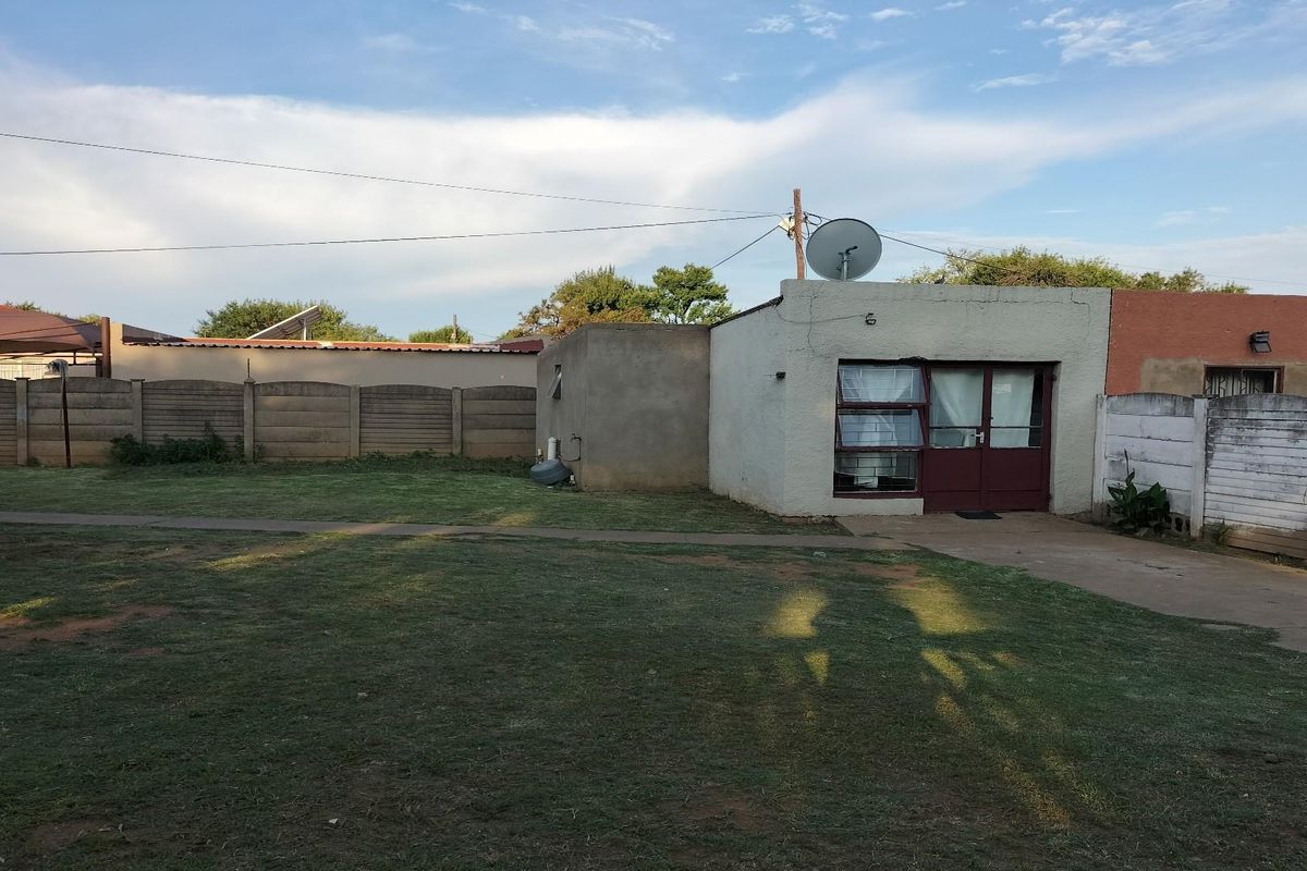 A view of the rear exterior of the property featuring a small structure, a paved walkway, and a large open grass area.