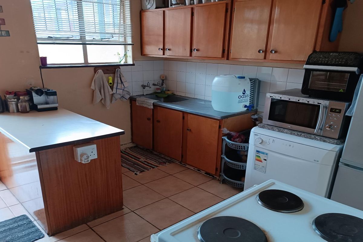 A functional kitchen featuring wooden cabinetry, tiled flooring, and a breakfast counter, offering a practical layout with space for essential appliances.