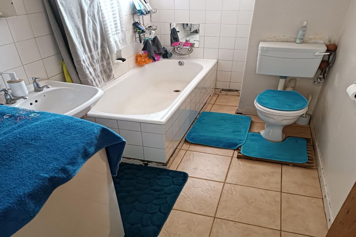 A dated bathroom featuring a standard bathtub, pedestal sink, and toilet with tiled walls and flooring, requiring cosmetic updates and maintenance.