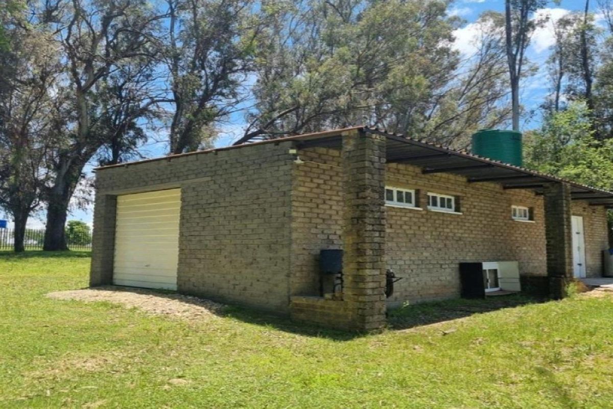 A detached brick outbuilding featuring a roller garage door, small windows, and an external water storage tank set within a grassy farm landscape.