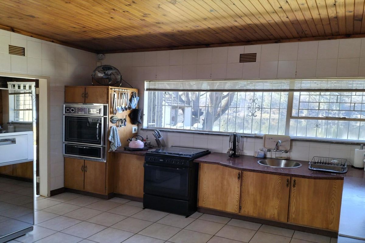 A dated kitchen featuring wood cabinetry, a built-in oven, a freestanding stove, and a large window overlooking the exterior grounds.
