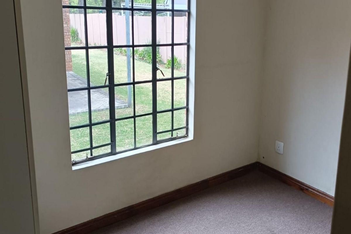 A vacant bedroom featuring neutral walls, carpeted flooring, and a large steel-framed window overlooking the rear garden area.