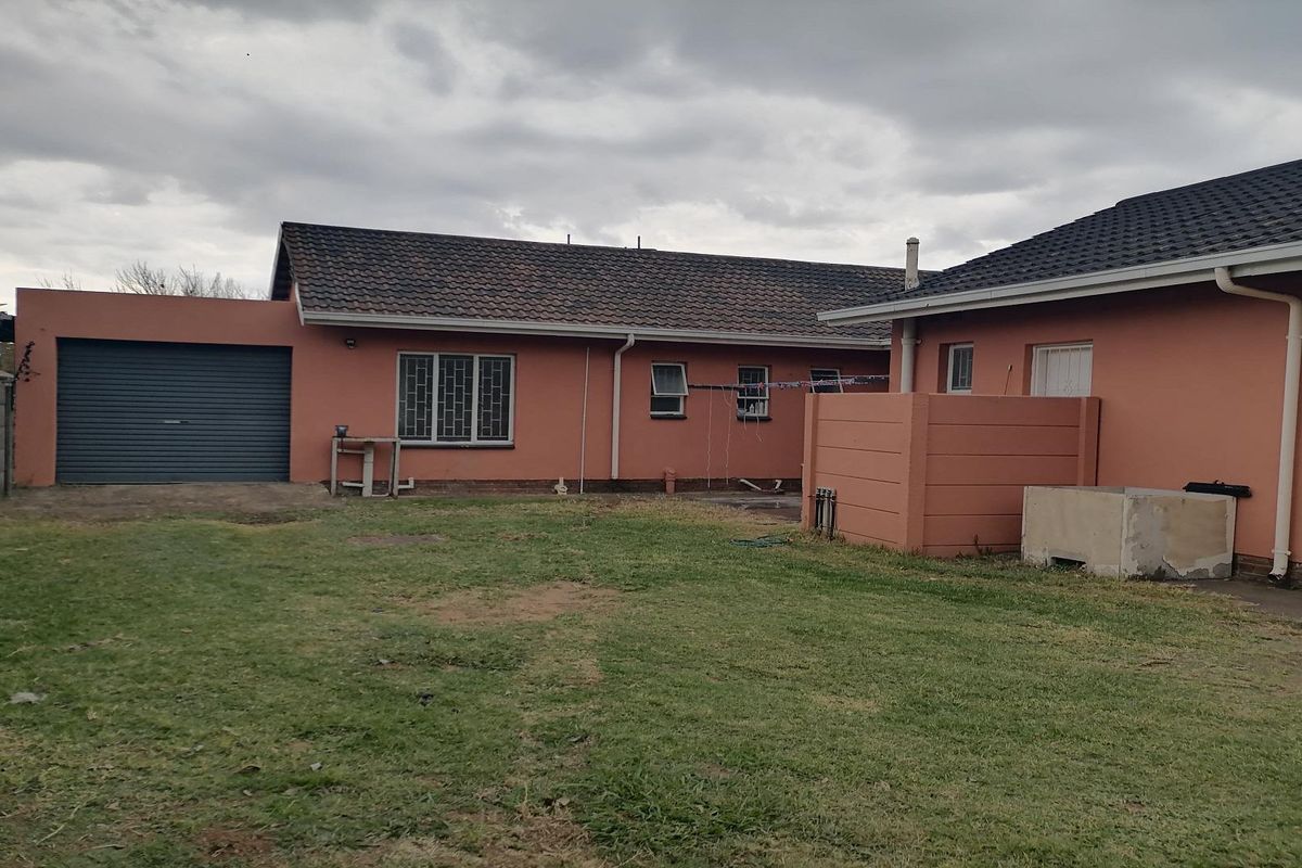 Rear view of the property featuring a spacious backyard, a single garage, and a low-maintenance exterior facade.